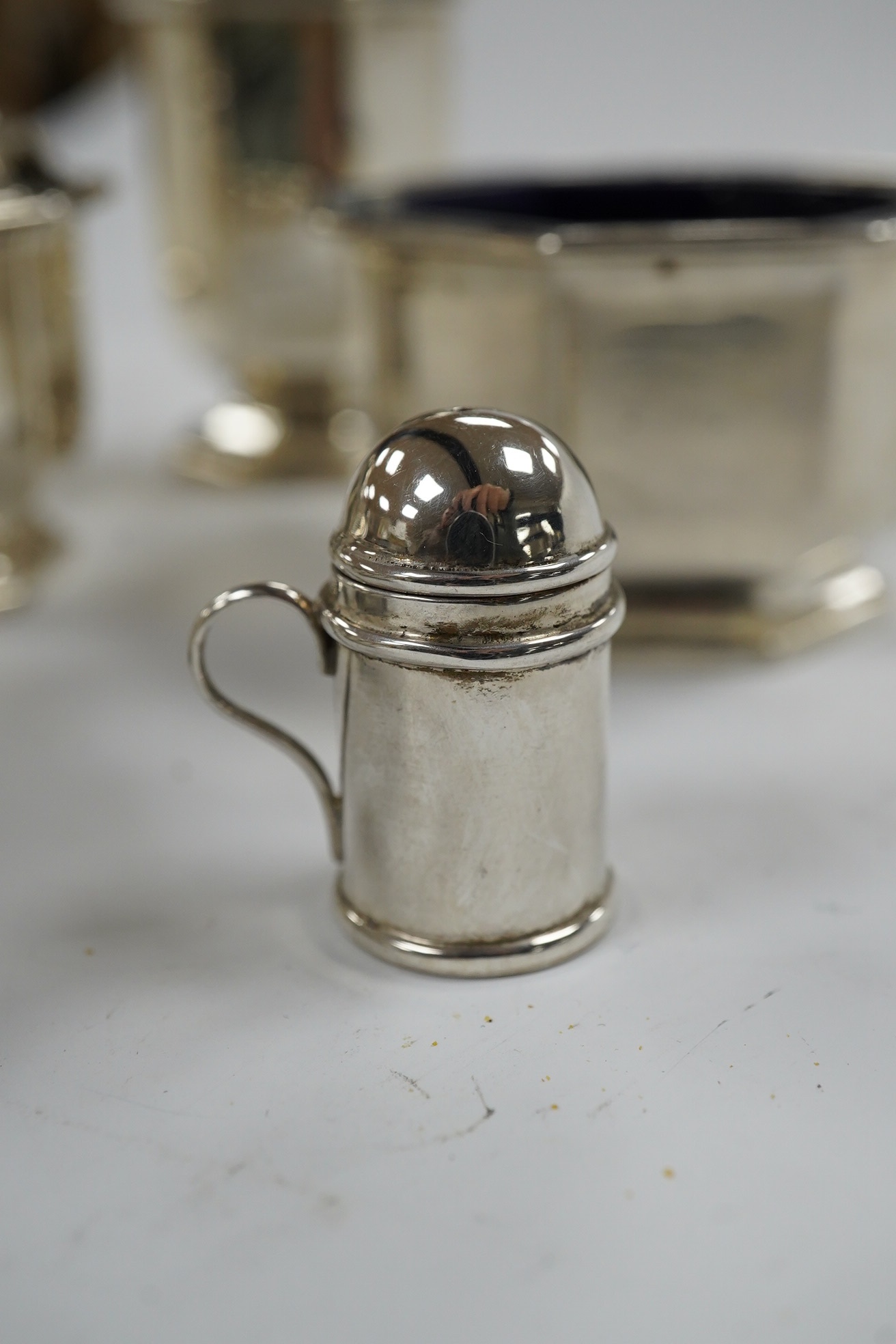 A George V five piece silver condiment set, Birmingham, 1931, two miniature 925 pepperettes and a silver shell salt. Condition - fair